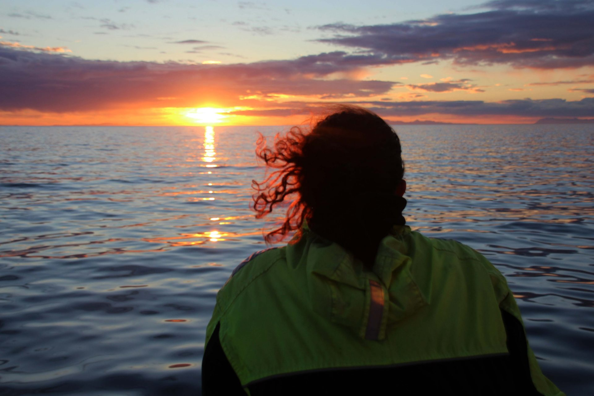 Person with curly hair overlooking ocean sunset