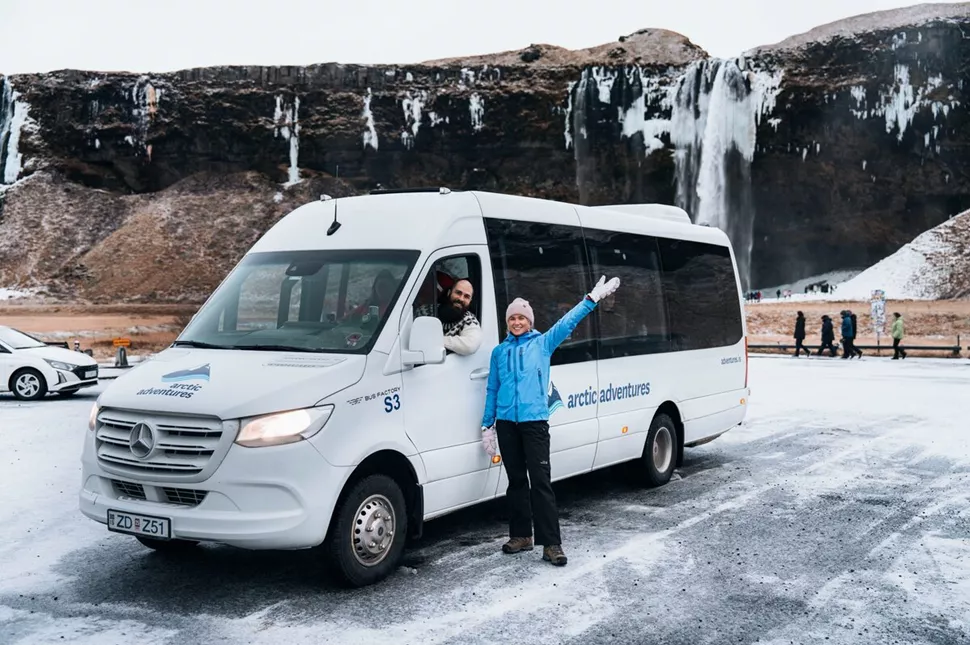 Woman waving by a white Arctic Adventures tour bus