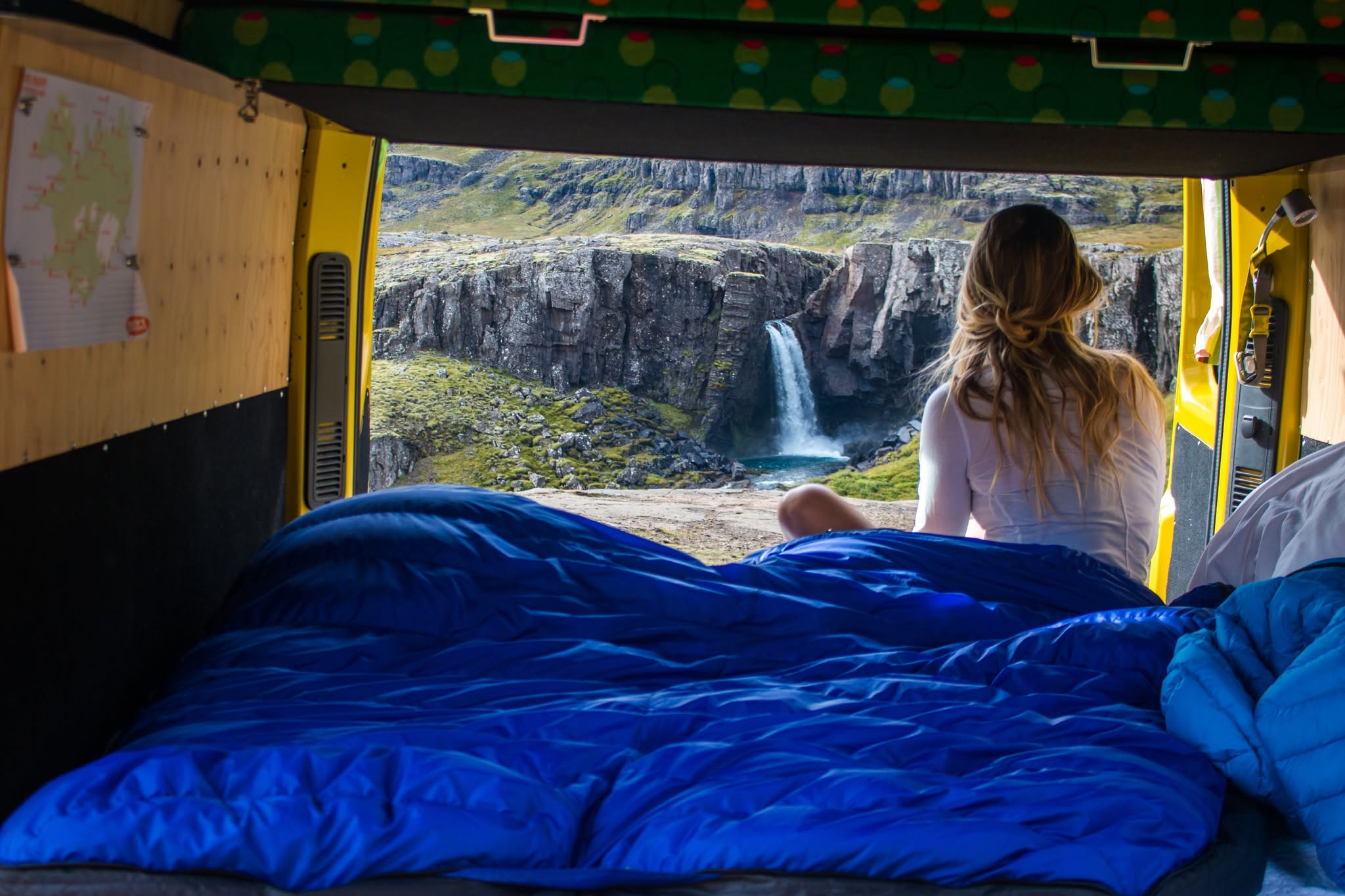 Woman sitting in camper van looking at waterfall.